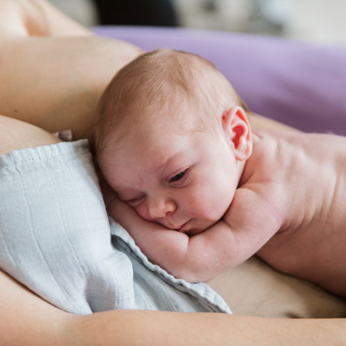 neonato appoggiato a pancia in giu sul seno della mamma