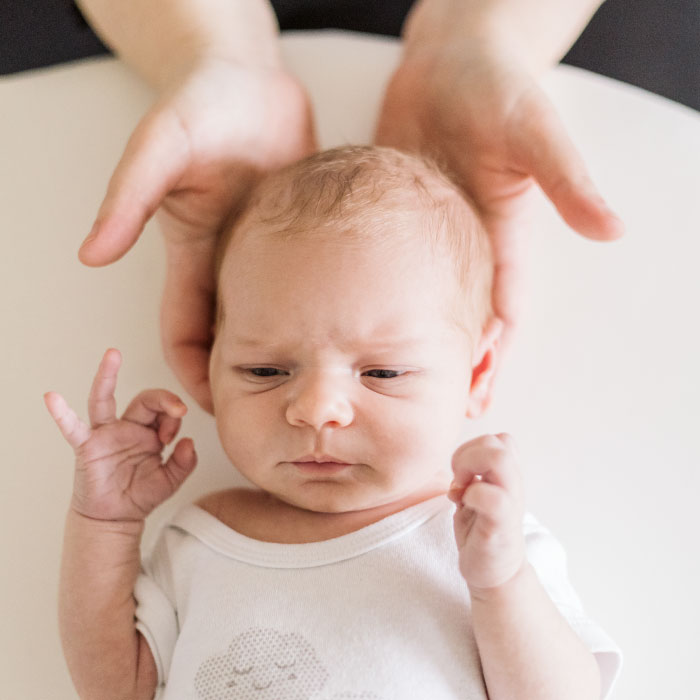 le mani dell'osteopata sorreggono delicatamente la testa di un bimbo di pochi mese sdraiato sulla schiena